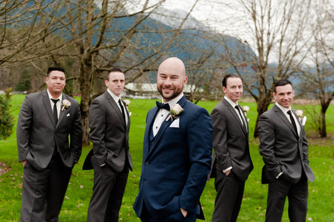 Wedding party properly co-ordinated with a groom standing out in a navy suit and groomsmen in matching charcoal suits