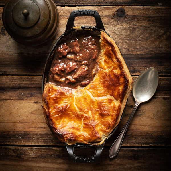 grant's Premium Stewed Steak cooked with a layer of puff pastry on top in a casserole dish on a wooden table.