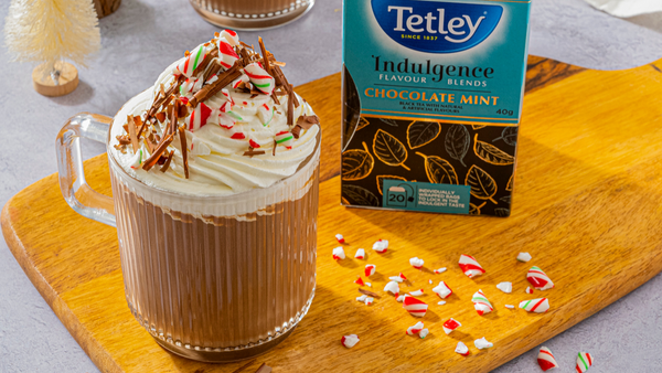 Tetley Chocolate Mint tea carton resting beside a latte topped with whipped cream and crushed peppermint candies