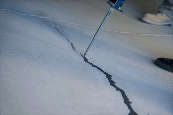 A person filling a concrete crack with epoxy