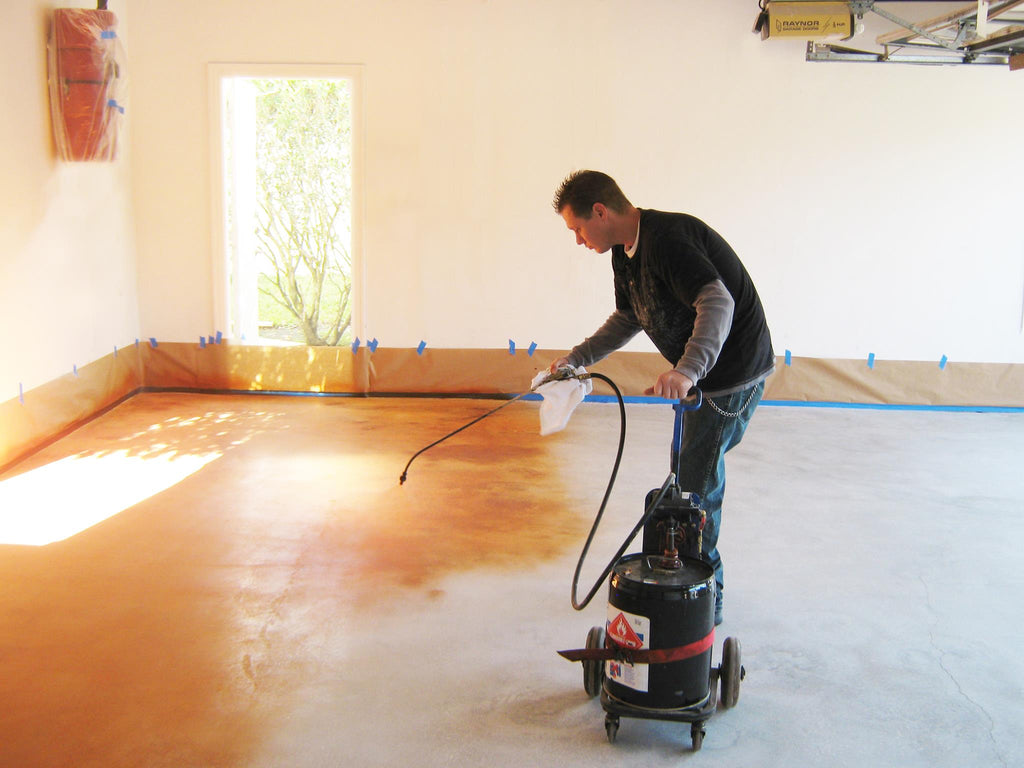 An installer applying a decorative concrete stain on a residential concrete garage floor by Xtreme Polishing Systems.