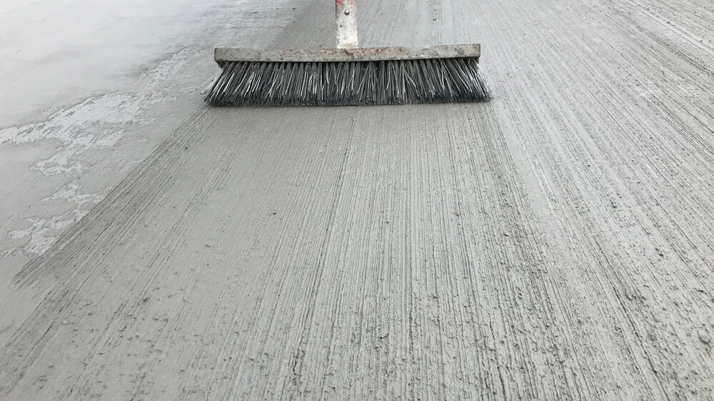 broom sweeping against wet concrete floor showing streaks in wet concrete