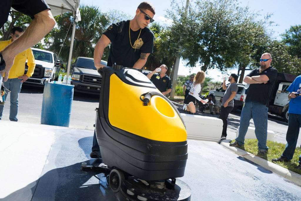 A person is cleaning a concrete slab with a walk-behind Genie Magic auto floor scrubber made by Xtreme Polishing Systems.