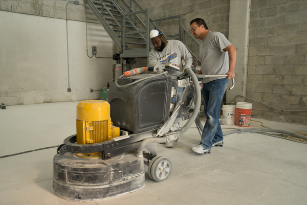 An image of two male contractors using a heavy-duty concrete floor grinder machine to grind a concrete floor surface.