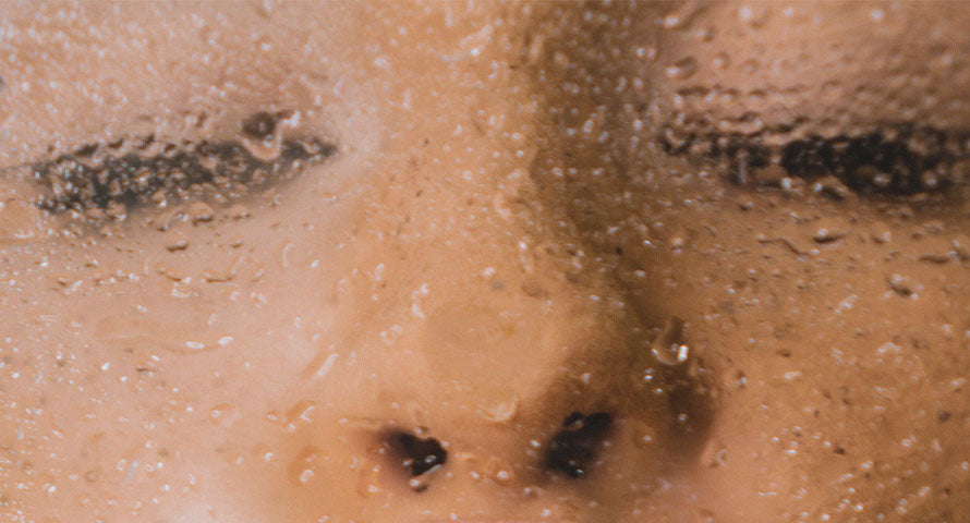 A close-up image of a woman's face viewed behind a glass pane covered in steam droplets, creating a blurred and atmospheric effect.