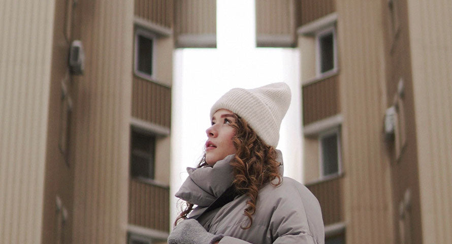 An image of a woman dressed in cozy winter attire, gazing upwards towards the sky, capturing a sense of wonder and the crispness of the winter season.