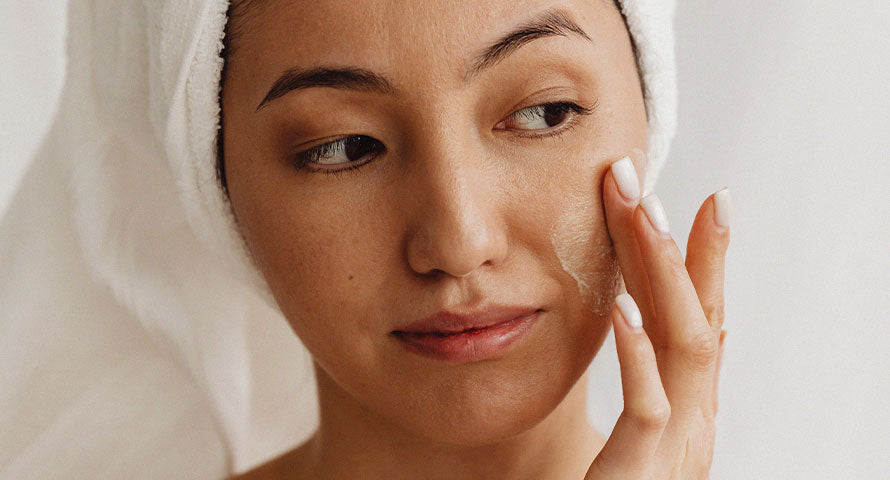 A close-up image of a woman's face with a head towel wrapped around her hair, demonstrating a skincare routine focused on cleansing and self-care.