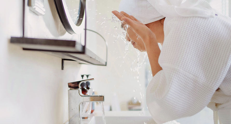 A dynamic image of a woman washing her face, her hands gently splashing clear water on her skin, symbolizing the purity and refreshing start of a skincare routine.