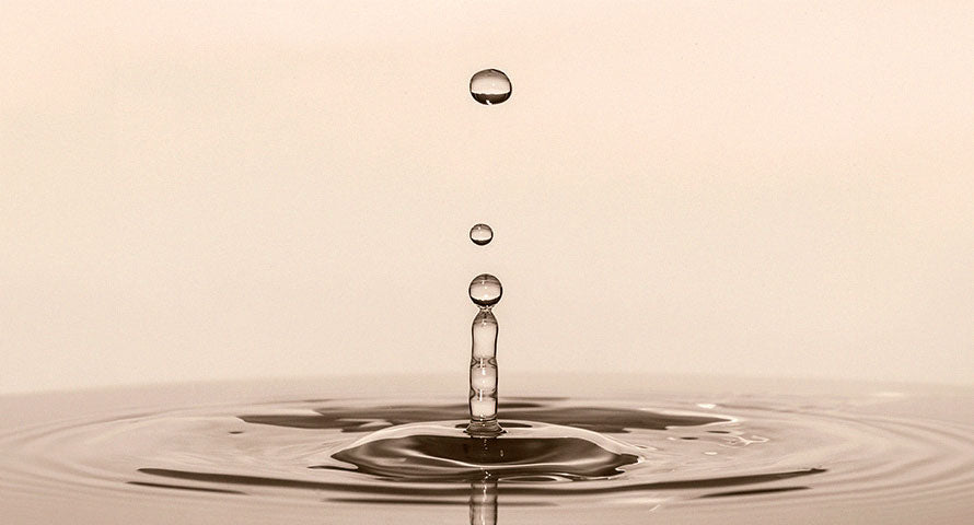 A close-up of a single water droplet, creating ripples and forming water drips, symbolizing the beauty and tranquility of nature's elements.