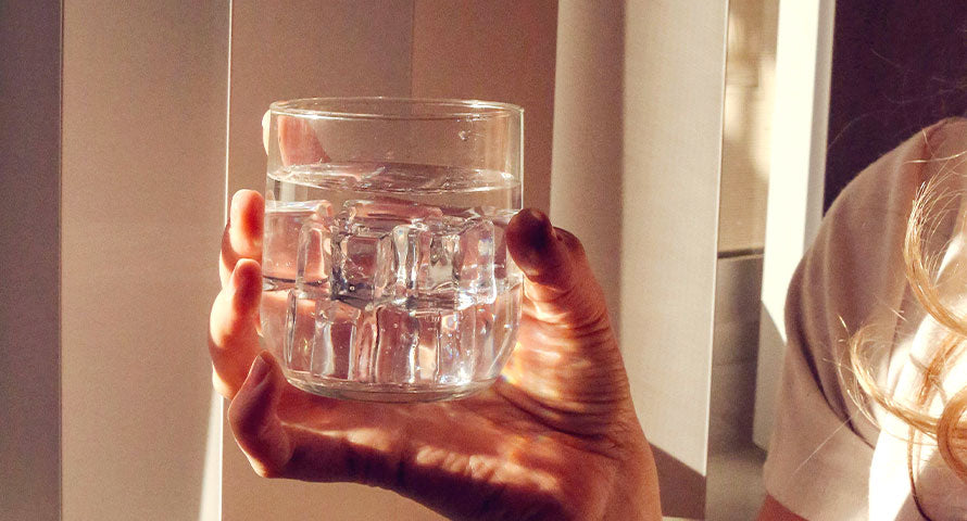 A hand holding a glass of water, representing hydration and skincare wellness, essential for achieving glowing and healthy skin.