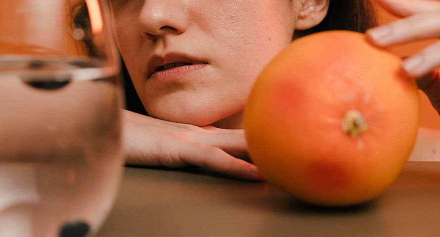 Woman holding an orange, symbolizing the importance of vitamin C in promoting healthy skin and collagen production.