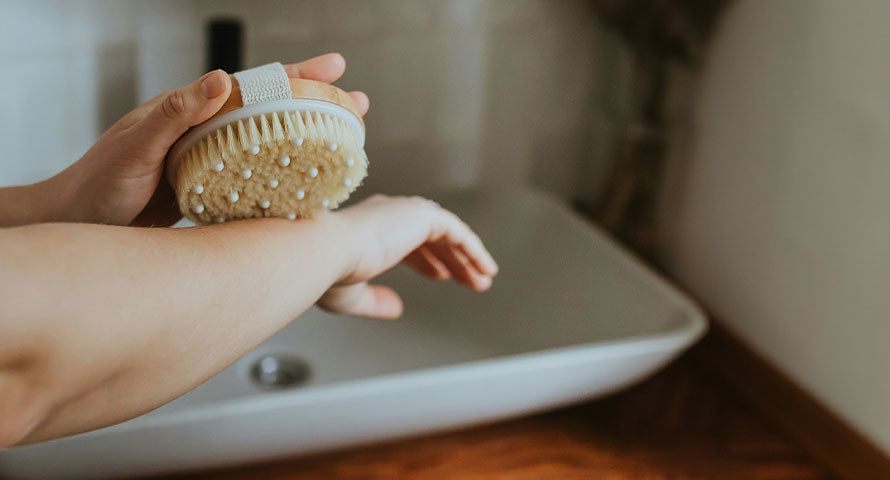 Image of a woman performing dry brushing on her skin to exfoliate and stimulate circulation, enhancing skin health and texture.