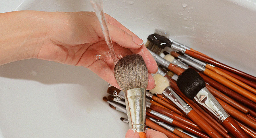Hand washing makeup brushes in soapy water, showcasing a key step in maintaining skincare hygiene.