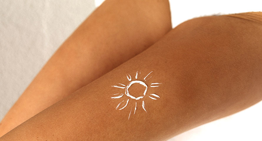 Close-up image of a woman's leg with a sun symbol drawn on it using sunscreen, emphasizing sun protection and skin care
