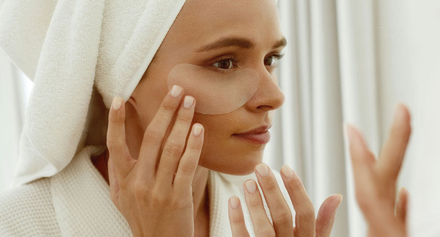 A woman applying an eye gel patch under her eye, focusing on her skincare routine for a refreshed and rejuvenated look.