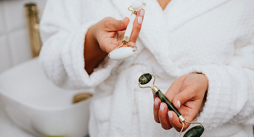 A woman holding two jade face rollers in her hand, ready to use them as part of her skincare routine.