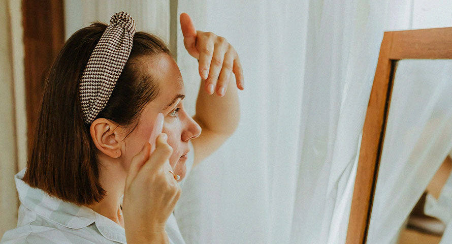 A woman gently using a gua sha tool on her face, following the contours of her skin to promote relaxation and enhance her skincare routine.