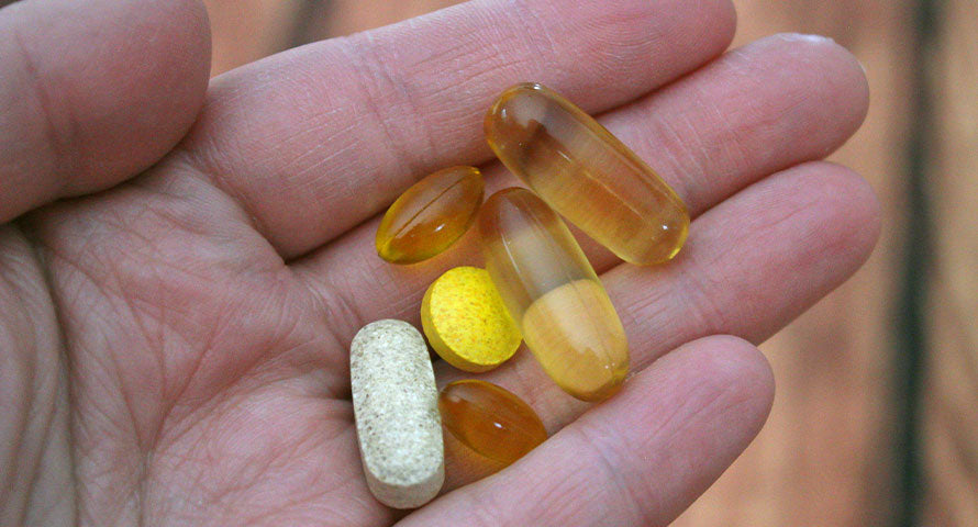 Close-up image of a hand holding a variety of colorful nutritional supplements.