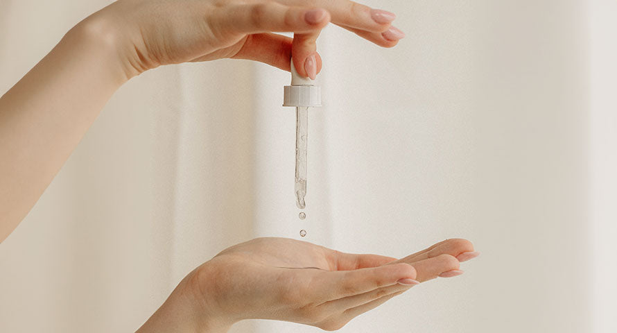 Close-up image of a hand holding a dropper and dispensing serum drops onto another hand, highlighting the texture and viscosity of the skincare serum against the skin.