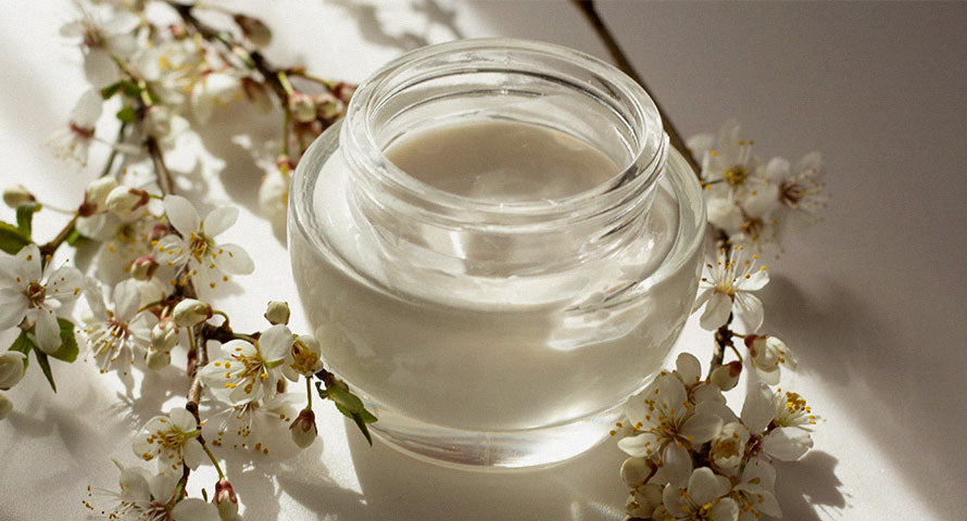 Image of a bottle of cream placed next to delicate spring flower blossoms, highlighting the natural ingredients in the skincare product and its connection to the freshness and beauty of spring.