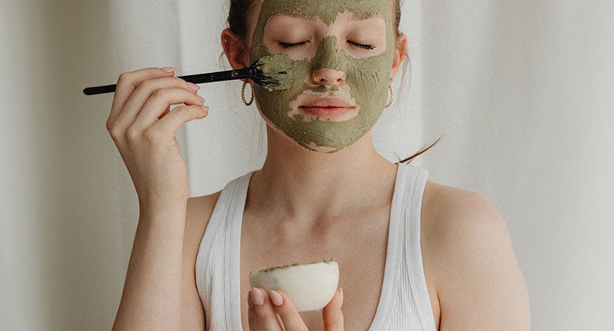 Image of a woman applying a green facial mask, illustrating a self-care routine with a focus on natural skincare, highlighting the fresh, vibrant color of the mask that suggests its natural ingredient composition.