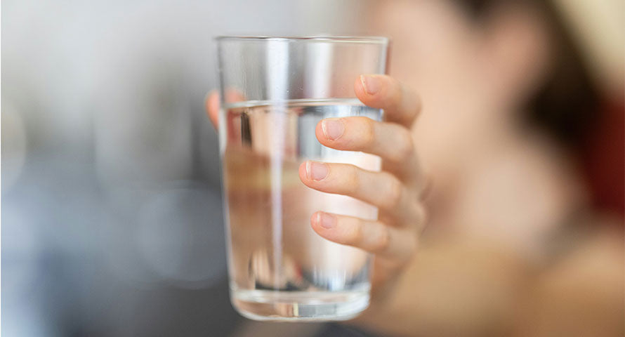 Close-up image of a hand holding a glass of water, symbolizing the importance of hydration for maintaining healthy skin, with a focus on the clear, refreshing quality of the water.