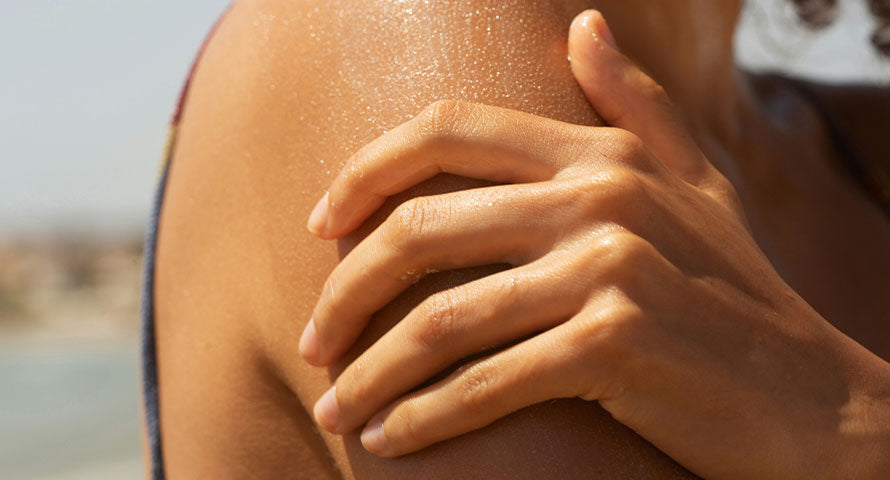 Image of a woman carefully applying sunscreen to her shoulder, showcasing the recommended technique for ensuring complete and effective coverage against UV radiation.