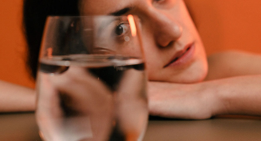 Image of a woman looking directly into the camera through a glass of water, creating a distorted and refractive visual effect on her face.