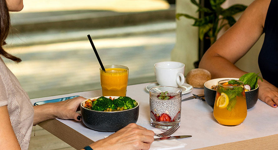  Image of a woman sitting at a table, enjoying a healthy meal consisting of a fresh salad and a glass of fruit juice, emphasizing a balanced and nutritious diet in a bright, casual dining setting.