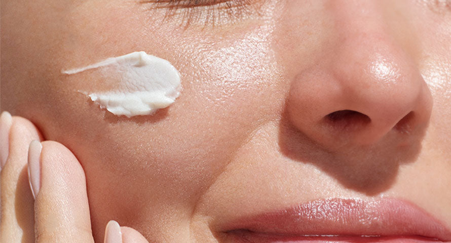 Woman applying cream on her cheek, focusing on skincare treatment.