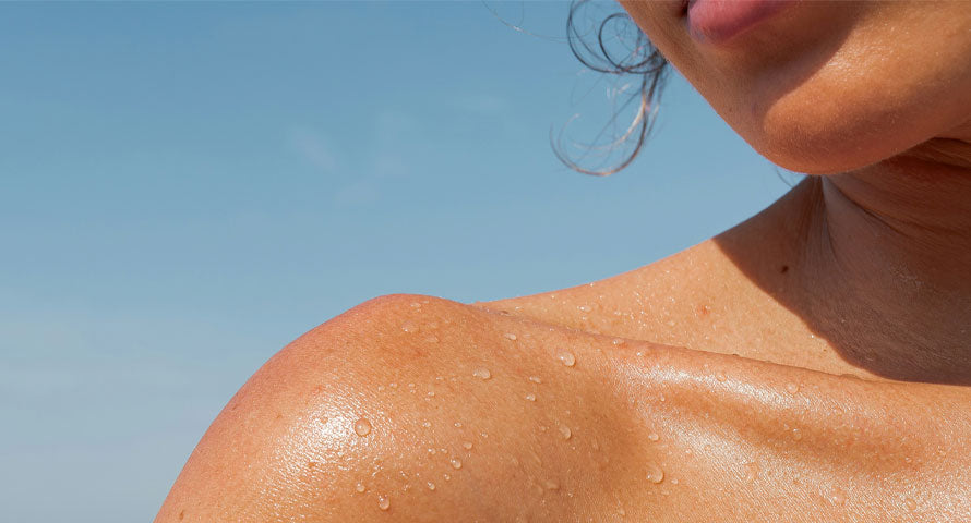 Detailed close-up of a woman's shoulder dotted with sweat beads, showcasing the humid summer conditions.