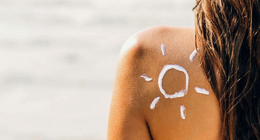 Image of a woman with a sunscreen-drawn sun shape on her shoulder, emphasizing the importance of sun protection in skincare routines.