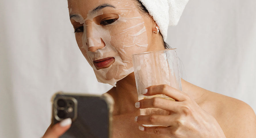 A woman wearing a protective face mask while drinking water, illustrating healthy lifestyle choices that complement urban skincare routines.