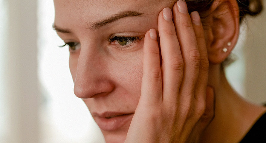 Concerned woman holding her cheek, reflecting on potential skin issues caused by urban environmental stressors.