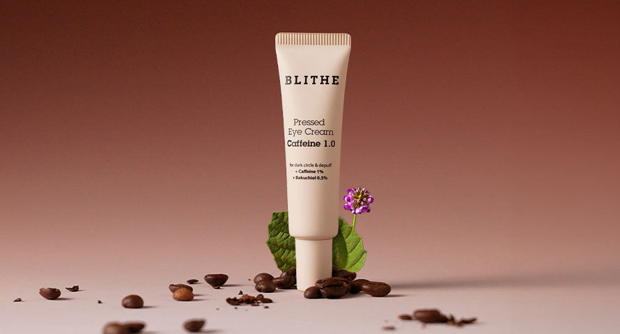 Blithe Eye Cream container placed alongside coffee grains, showcasing the product's association with caffeine, a key ingredient known for its benefits in reducing puffiness and dark circles.