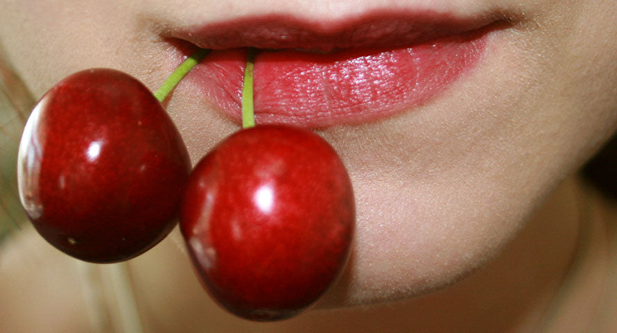 Close-up of a woman's lips holding a cherry, capturing the essence of the Cherry Cola Lips trend, a popular 2023 beauty style on TikTok.