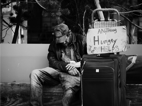 Homeless guy sitting by a suitcase with a sign saying "Anything helps....Hungry"