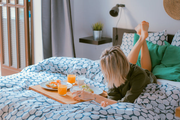 Frau liegt im Bett liest ein Buch und trinkt etwas