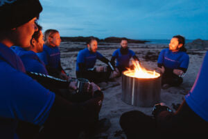 close up of team of adventurers sat around a campfire on the beach