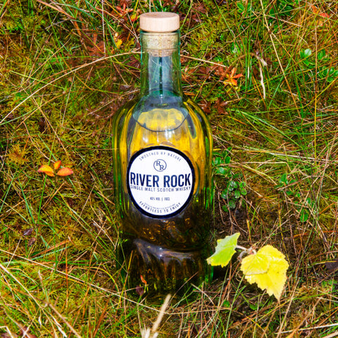 Bottle of river rock single malt whisky laid on the grass