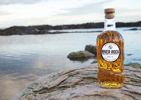 Bottle of single malt River Rock whisky on a rock next to a Scottish river