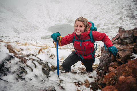 Woman wearing red jacket smiling for photo whilst climbing up a mountain