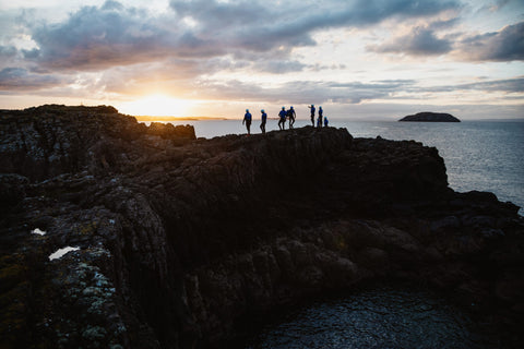 group of people in the distance standing on the coastal rock at sunset