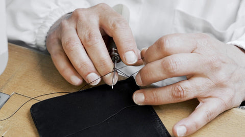 Artisan hands meticulously hand-stitching a black leather piece with a needle and thread, exemplifying Trevony's dedication to traditional craftsmanship in their luxury products.