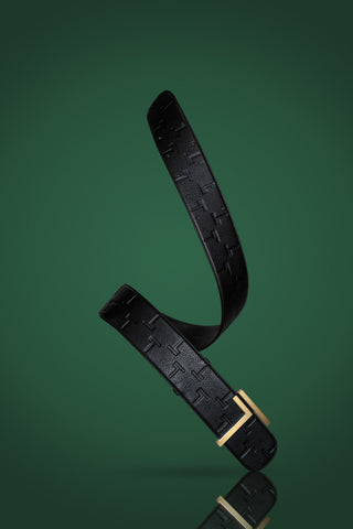 The Trevony Truth Oversized Belt is elegantly displayed against a deep green background, highlighting its luxurious black calfskin leather with an embossed pattern and a polished gold-tone buckle. The belt is artistically curved, showcasing its texture and the reflective sheen of its sophisticated hardware.