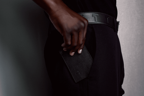 A person in an elegant black outfit subtly pockets the Trevony Vinny Bill Clip wallet, showcasing the fine texture and discreet branding of this luxury accessory. The wallet’s refined design and the wearer's sleek attire combine to depict a lifestyle of understated sophistication.