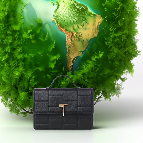 Medium Minerva handbag by Trevony in black leather, featuring a distinctive grid pattern and gold 'T' logo clasp, presented against a creative backdrop with a green, globe-shaped plant element.