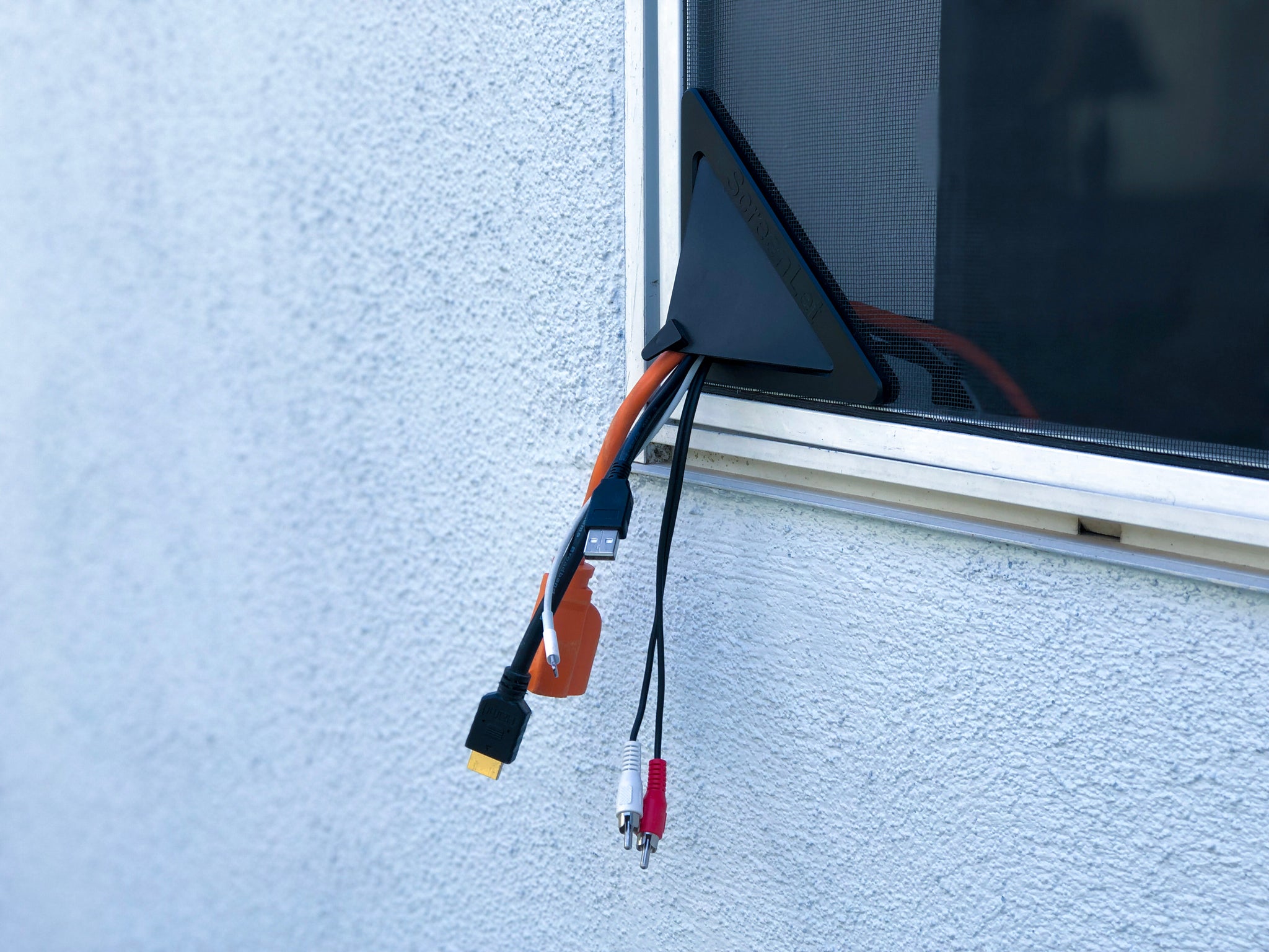 The ScreenLet system in use, showing a static setup with a cluster of cables extending through it, emphasizing the product's intended use as a fixed point of passage for cables, maintaining window screen integrity and simplifying outdoor power access