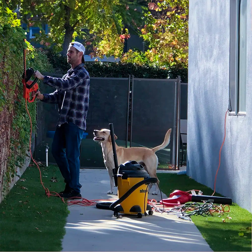 Hombre usando herramientas eléctricas en el patio trasero con ScreenLet, junto a un perro juguetón