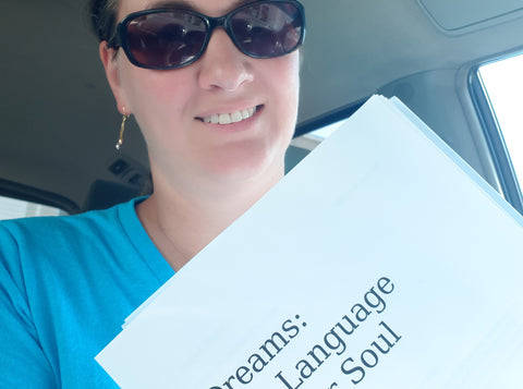 Close up of woman in blue shirt and sunglasses holding printed manuscript of upcoming book